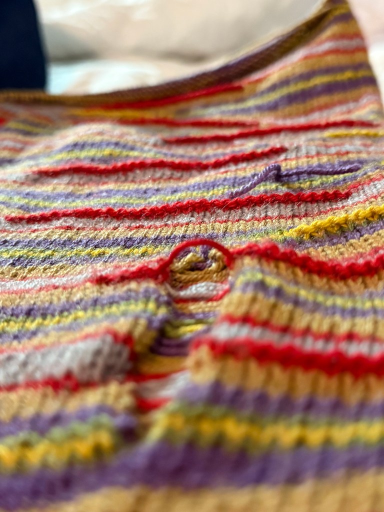 A close-up of a running hole added intentionally into the knit fabric, along with visible yarn tails left out from a knot-joined skein.