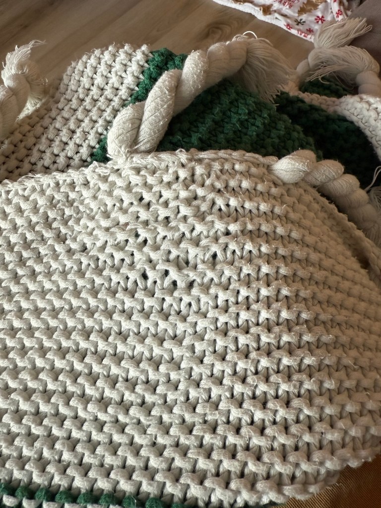 A close-up of the completed repair in the white knit section of the blanket. The stitches have been reworked and secured, with a few uneven areas but overall sturdy and continuous knitting across the green base.