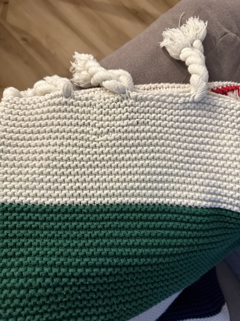 The finished Hudson’s Bay cotton blanket with thick white and green stripes. Repaired stitches are barely visible at the top edge. Decorative twisted tassels line the border, and the blanket lies smooth across a couch