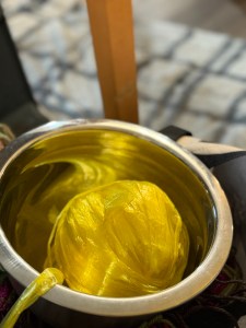 A ball of bright yellow plastic bag yarn (plarn) sits in a shiny metal bowl, used as a yarn holder.