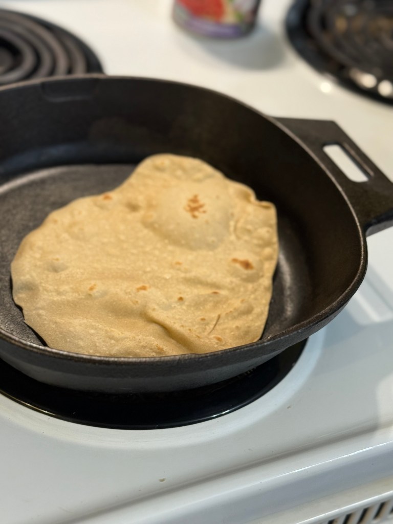 The roti in the cast iron skillet has started to puff and form golden brown spots, a sign that it’s nearly done.