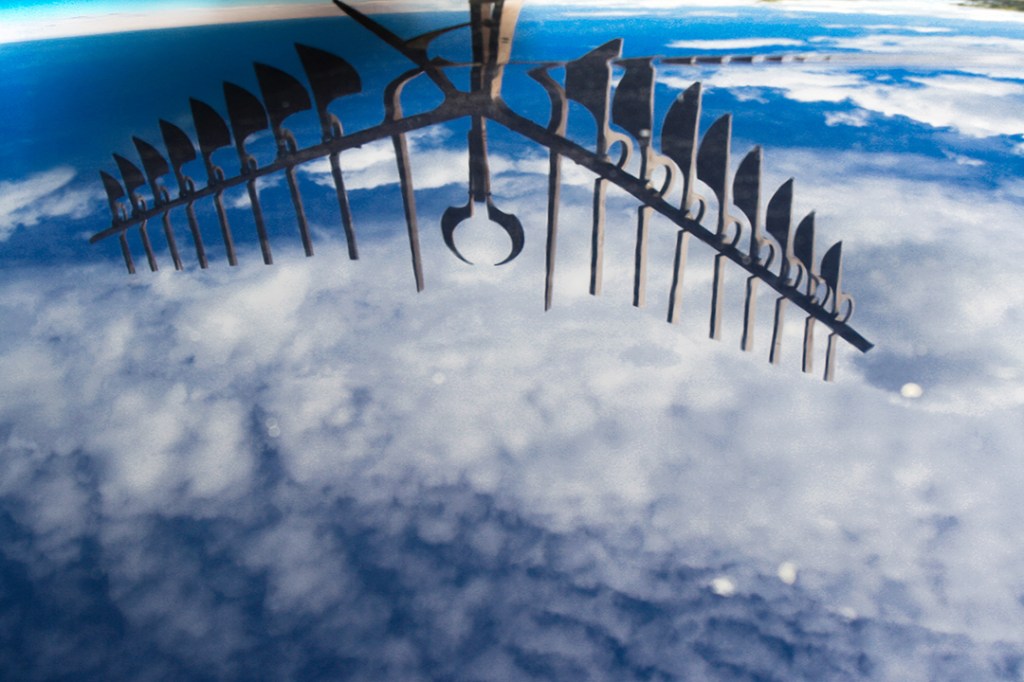 Reflection of the Spirit Catcher sculpture in Barrie, Ontario, captured on a smooth reflective surface, appearing as though it is floating in the clouds. THe image is distorted, short and long, in the top third of the image.